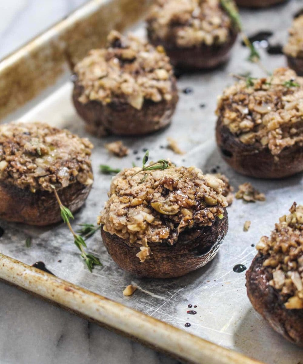 These Vegan Stuffed Mushrooms are a fast and easy party appetizer recipe with less than 10 ingredients! They are filled with nutty walnuts, salty olives, and fresh herbs and finished with a drizzle of sweet balsamic glaze. | CatchingSeeds.com
