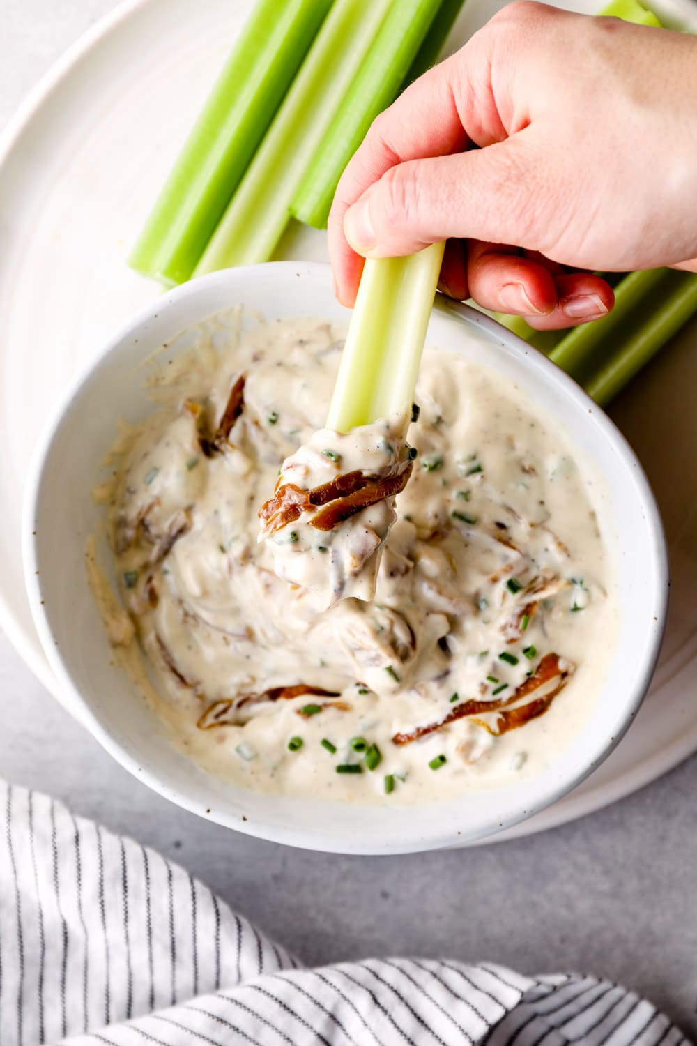 A piece of celery dipping into Vegan French Onion Dip.
