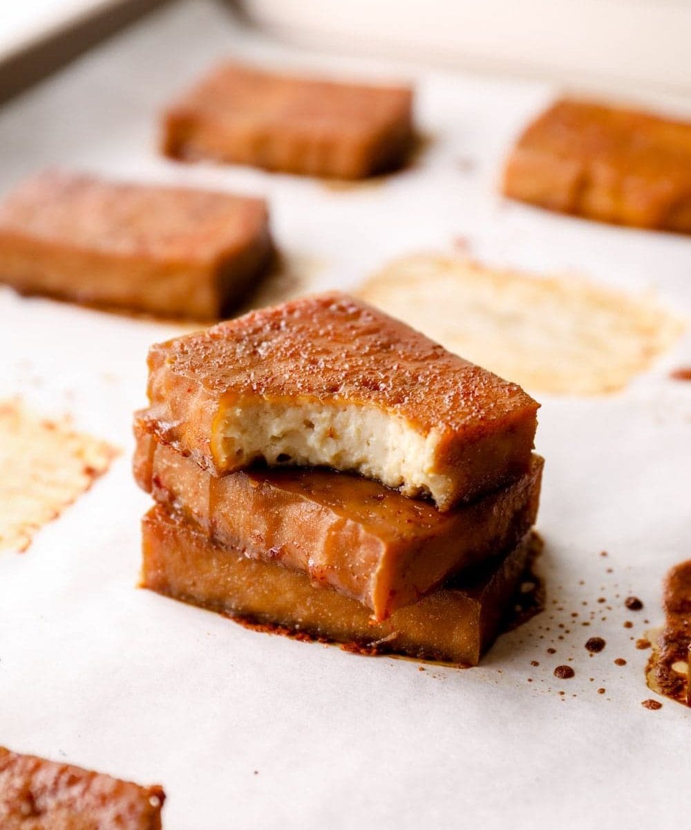 A stack of baked tofu with a bite out of the top piece.