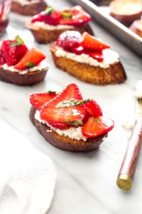 Four toasts with almond ricotta, strawberries, and basil.