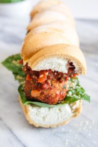 A vegan meatball sandwiches with marinara sauce and basil on a white roll.