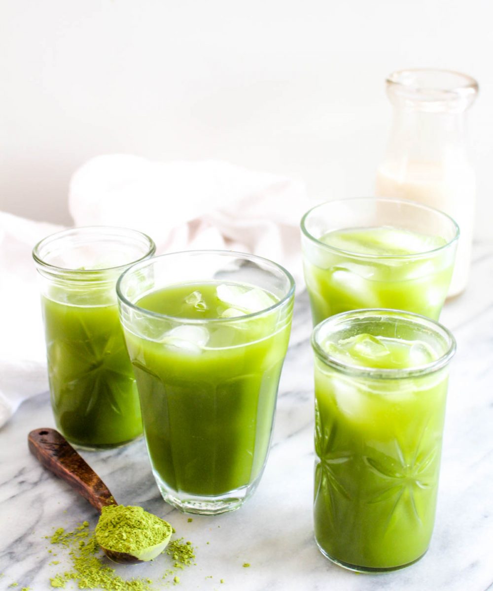 Four glasses of iced coconut water matcha with a spoonful of matcha tea on the side.