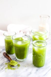 Four glasses of iced coconut water matcha with a spoonful of matcha tea on the side.