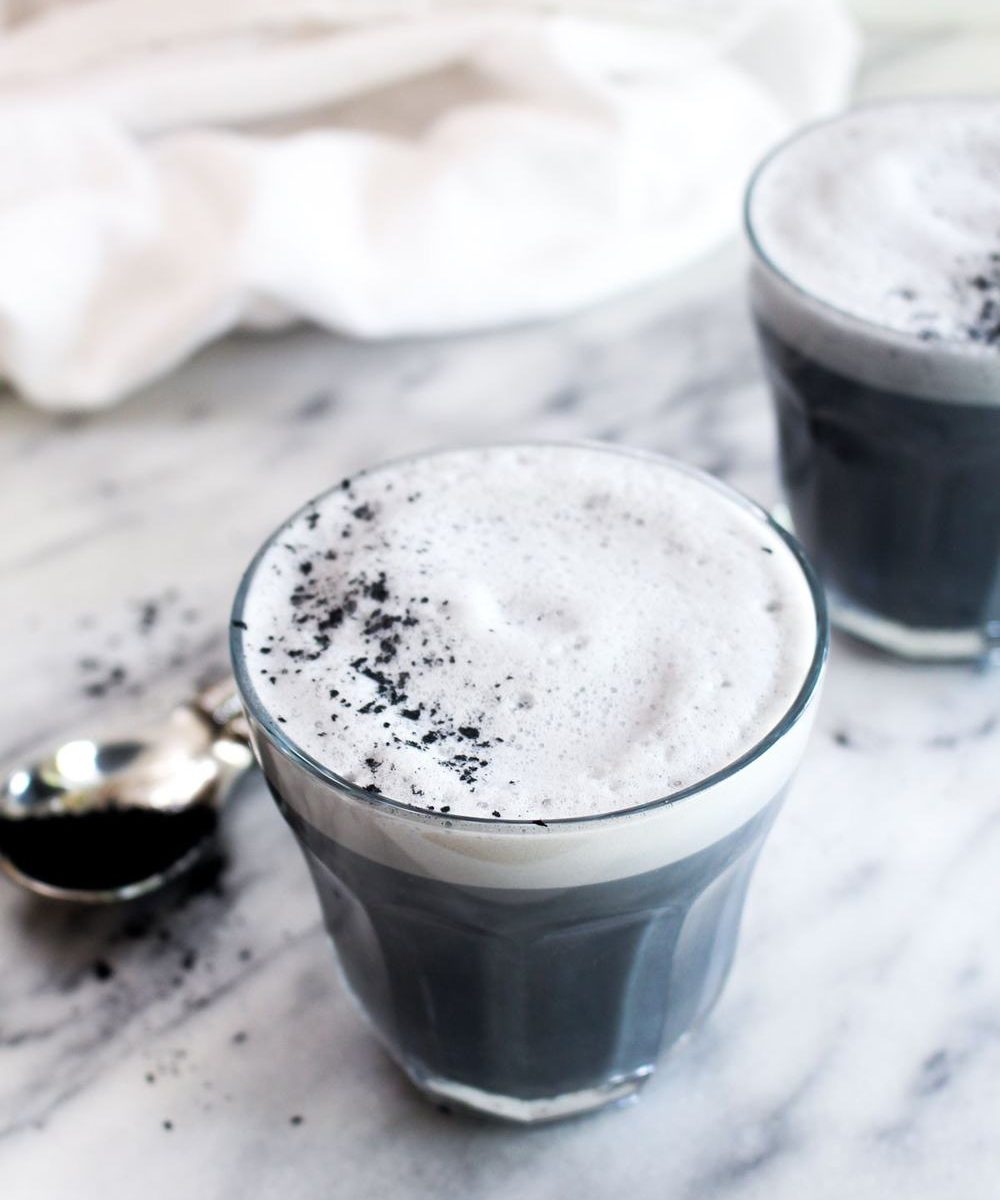 A three quarter view of a black charcoal latte with foam and charcoal sprinkled on top.