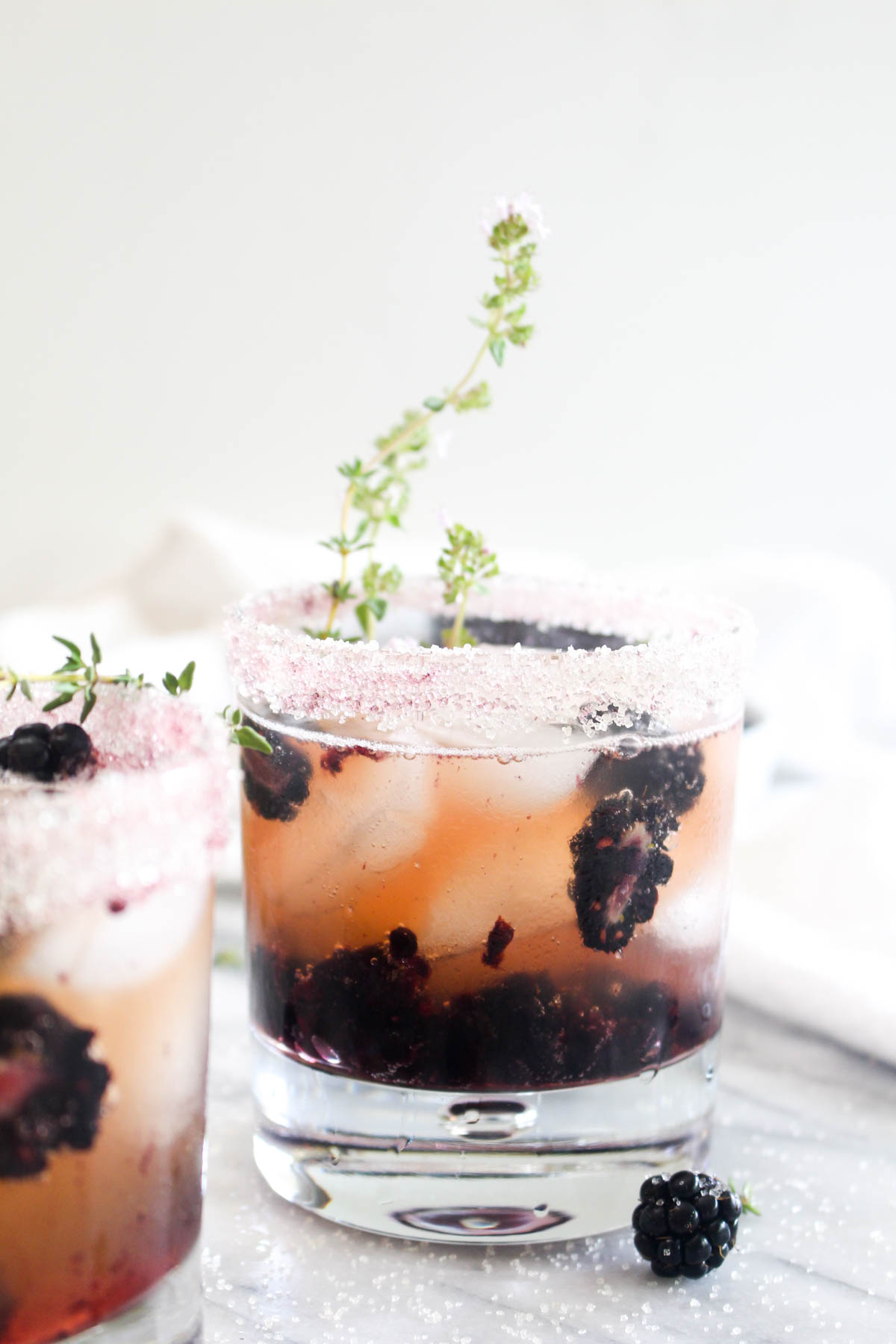 A glass filled with ice, blackberries, kombucha vodka smash, and thyme. 