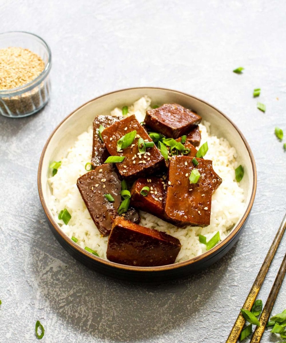 Maple Sriracha baked tofu over rice with chopsticks and scallions.