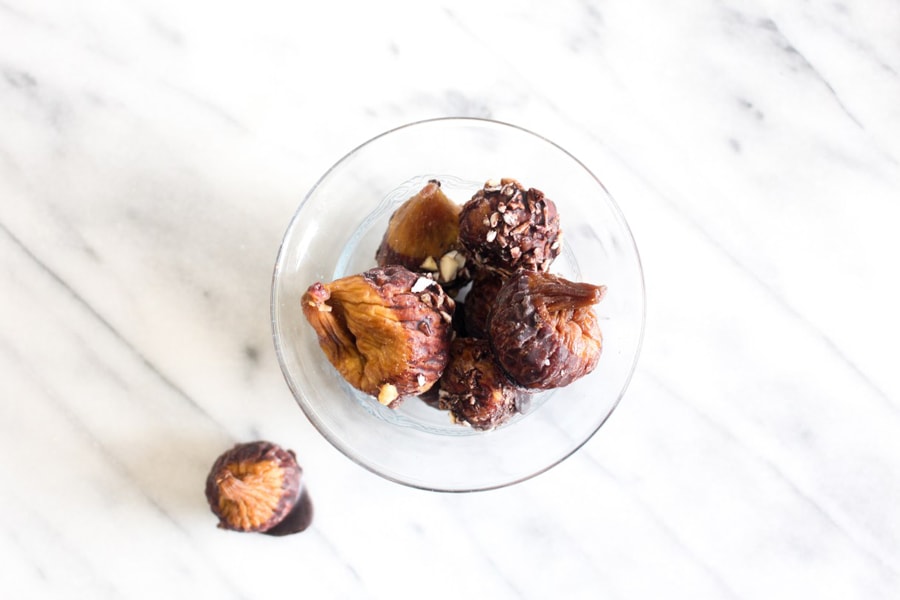 A clear bowl filled with dried figs dipped in vegan chocolate and nuts.