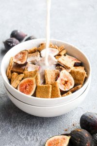 Milk being poured into a bowl of cereal with sliced figs.