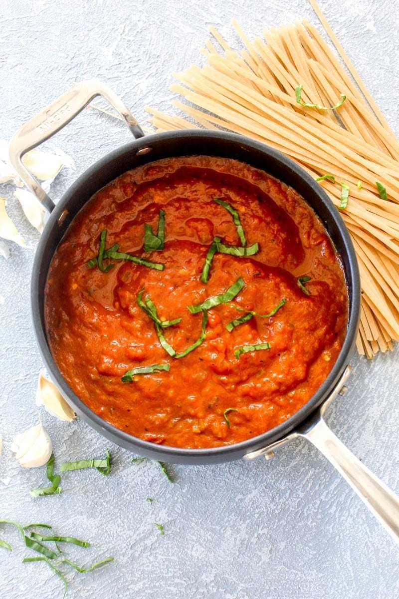 A pot of roasted red pepper pasta sauce with basil, garlic, and dry noodles.