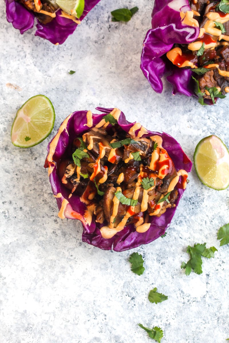 One Mushroom Tempeh Cabbage Cups with lime wedges, sriracha, and cilantro.
