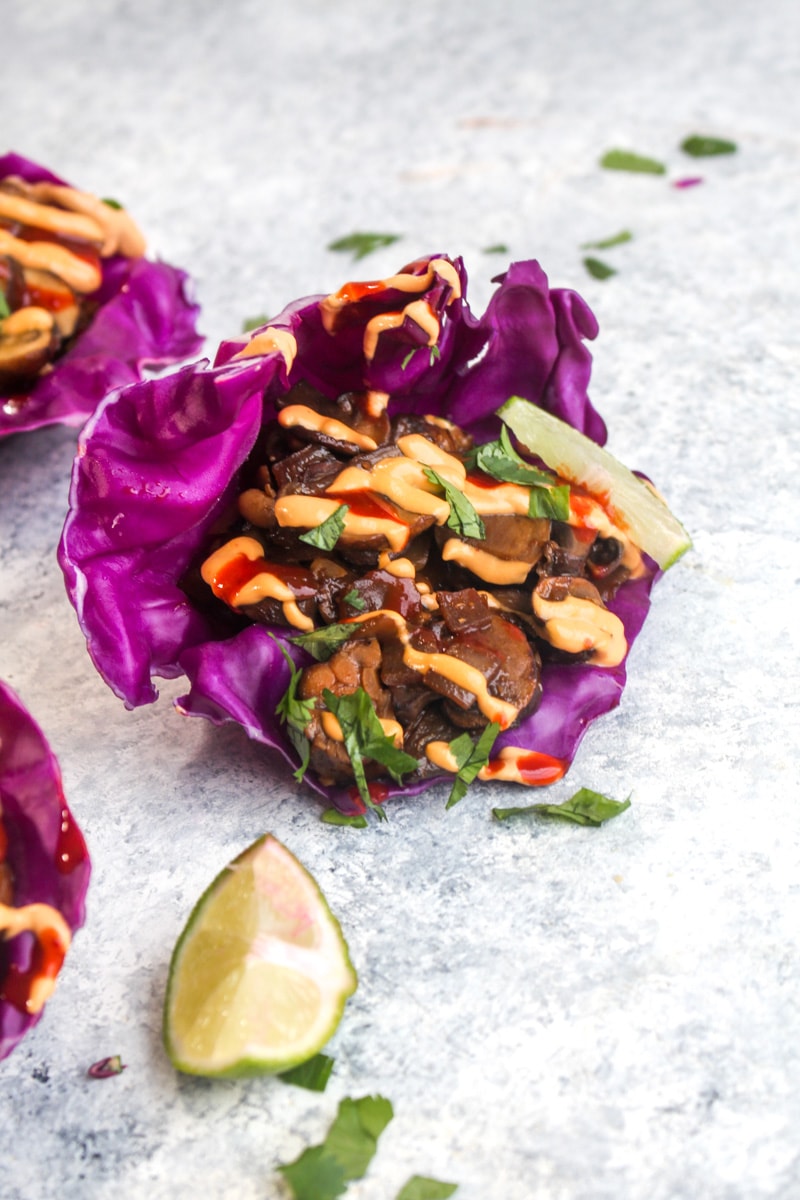 One Mushroom Tempeh Cabbage Cups with lime wedges, sriracha, and cilantro.