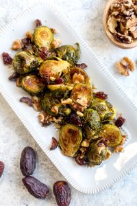 Roasted brussels sprouts on a white dish with dates and walnuts.