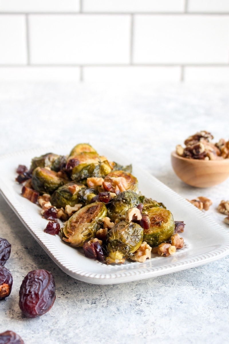 Roasted brussels sprouts on a white dish with dates and walnuts.