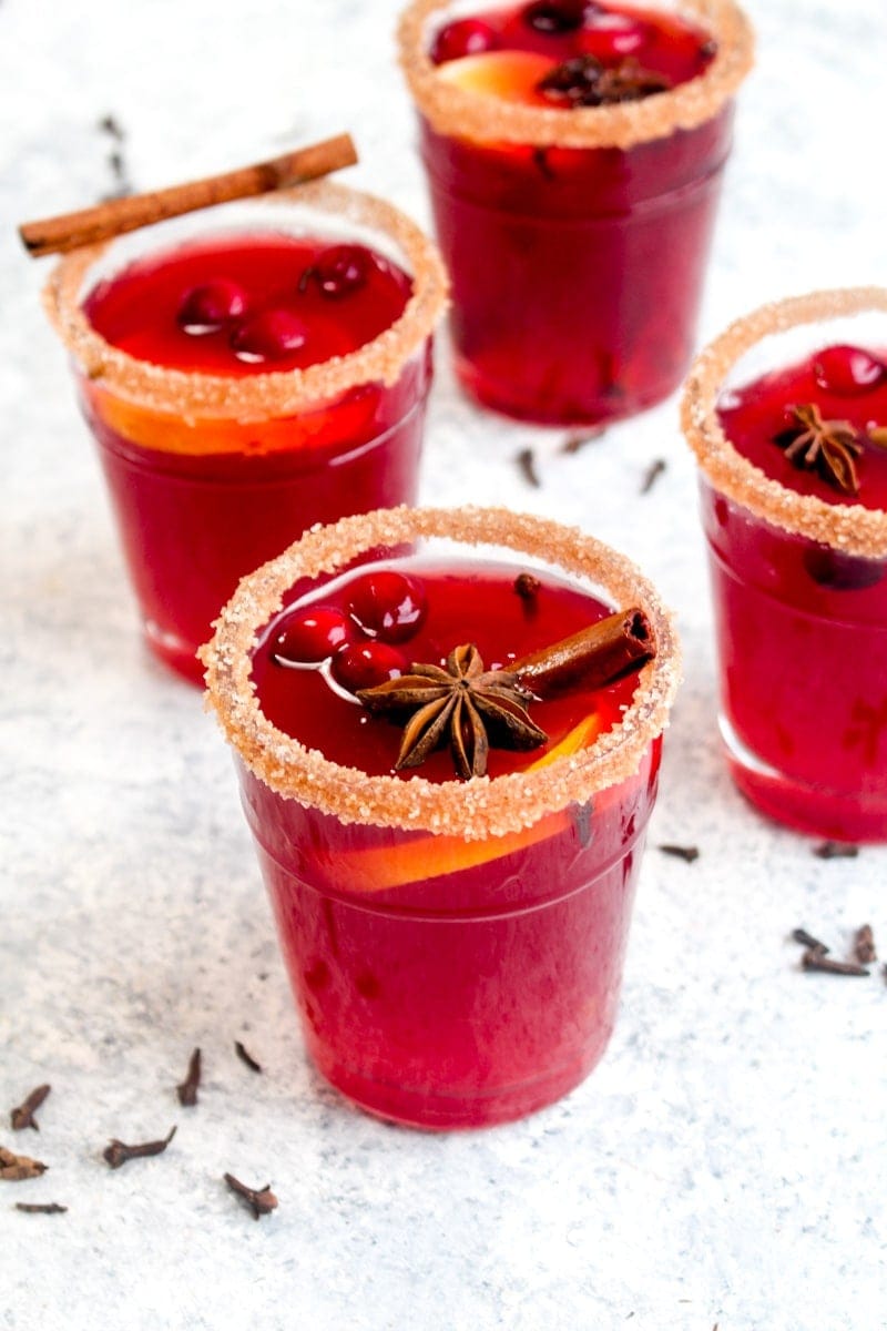 Four glasses of holiday spiced cranberry cocktail with orange slices and cinnamon sticks. 