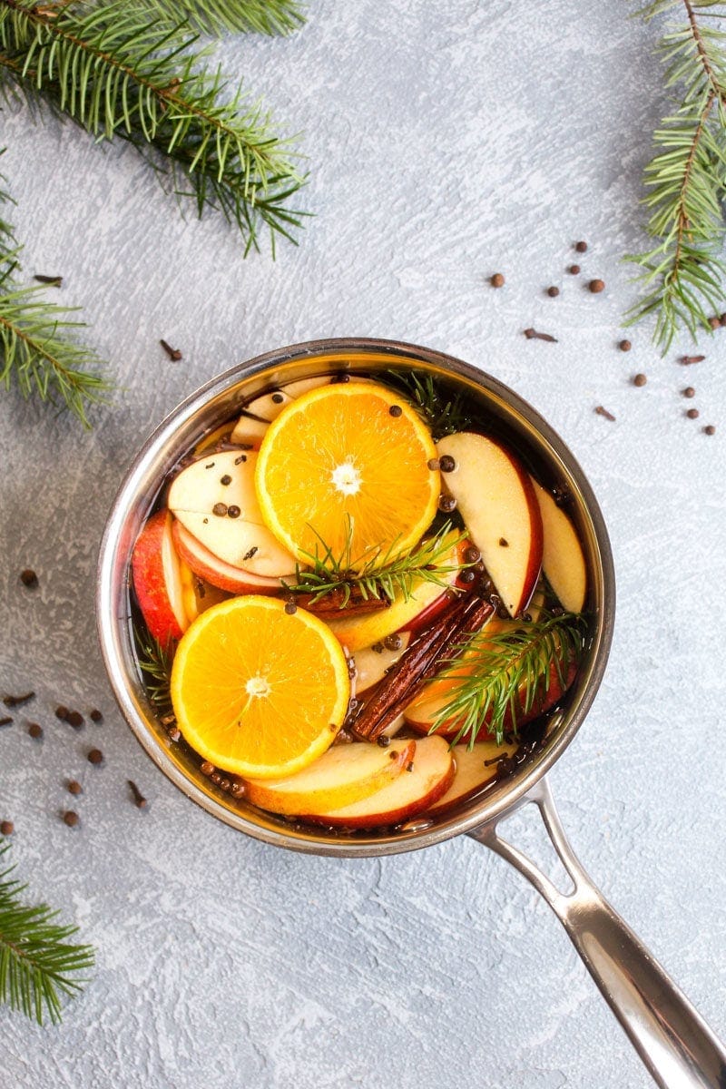 A silver pot filled with fresh christmas potpourri which is oranges, apples, cinnamon, cloves, allspice, and pine.