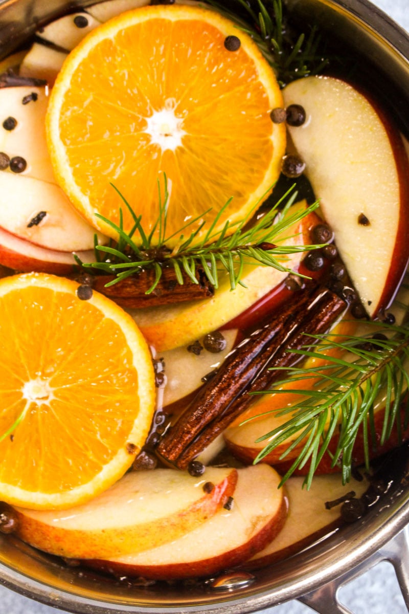 A closeup of fresh christmas potpourri which is oranges, apples, cinnamon, cloves, allspice, and pine.