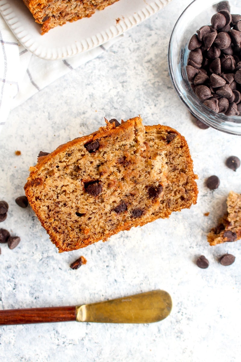 A slice of gluten free vegan chocolate chip banana bread on a grey background.