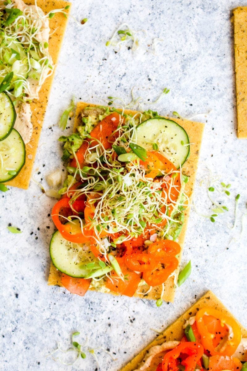 A grain free chickpea flatbread topped with avocado, cucumber, peppers, and sprouts.