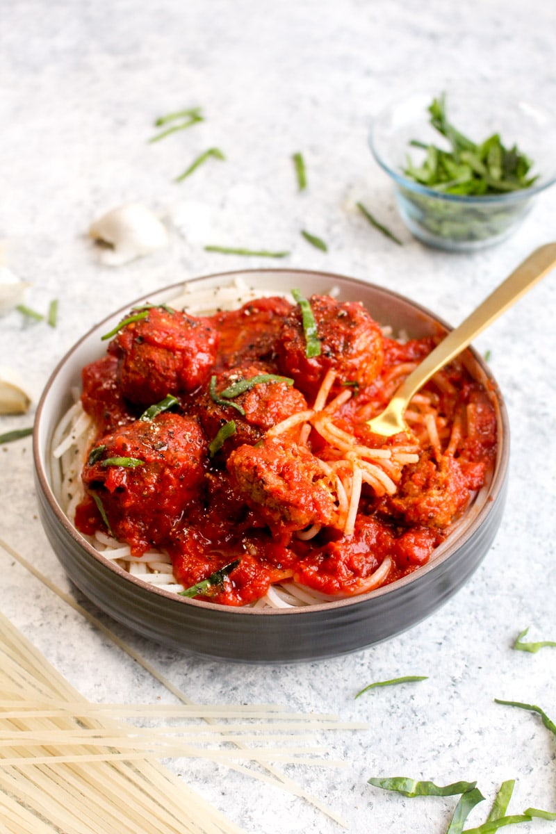 A bowl of freezer meal veggie meatballs over pasta with red sauce and a gold fork. 