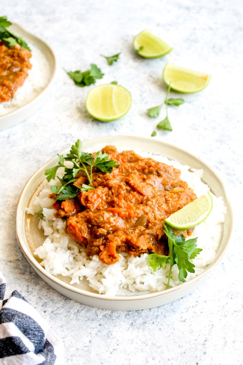 A plate topped with rice and red lentil sweet potato dahl with cilantro and lime.