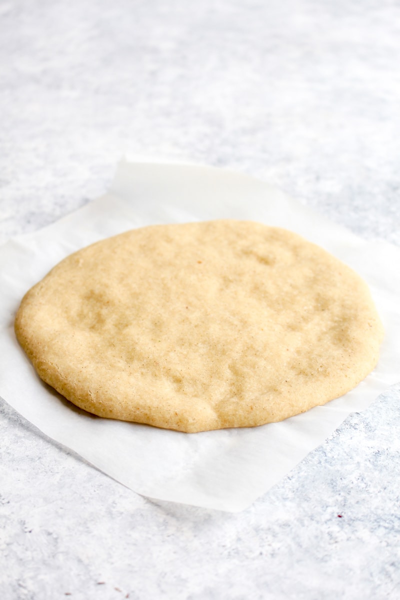 A baked gluten free pizza crust on a piece of parchment paper.
