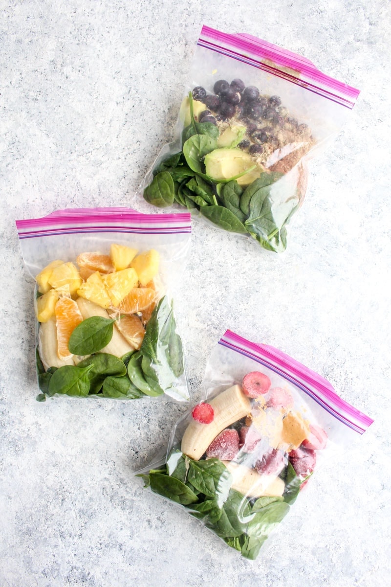 Three freezer smoothie packs filled with fruit and spinach. 