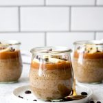 Three jars of caramel macchiato chia pudding topped with caramel sauce, bananas, and cacao nibs.