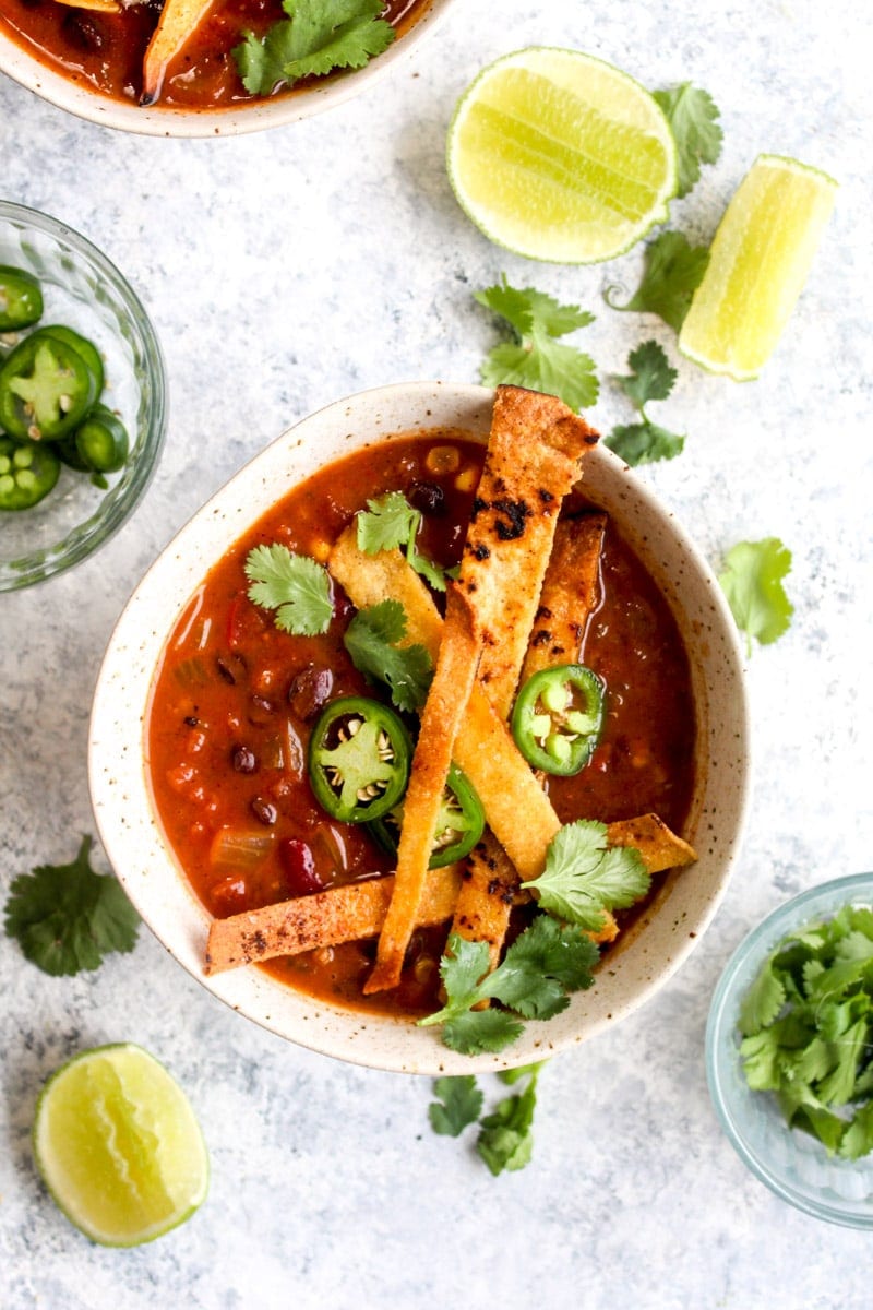 A bowl of vegan tortilla soup topped with tortilla strips and jalapeno slices.