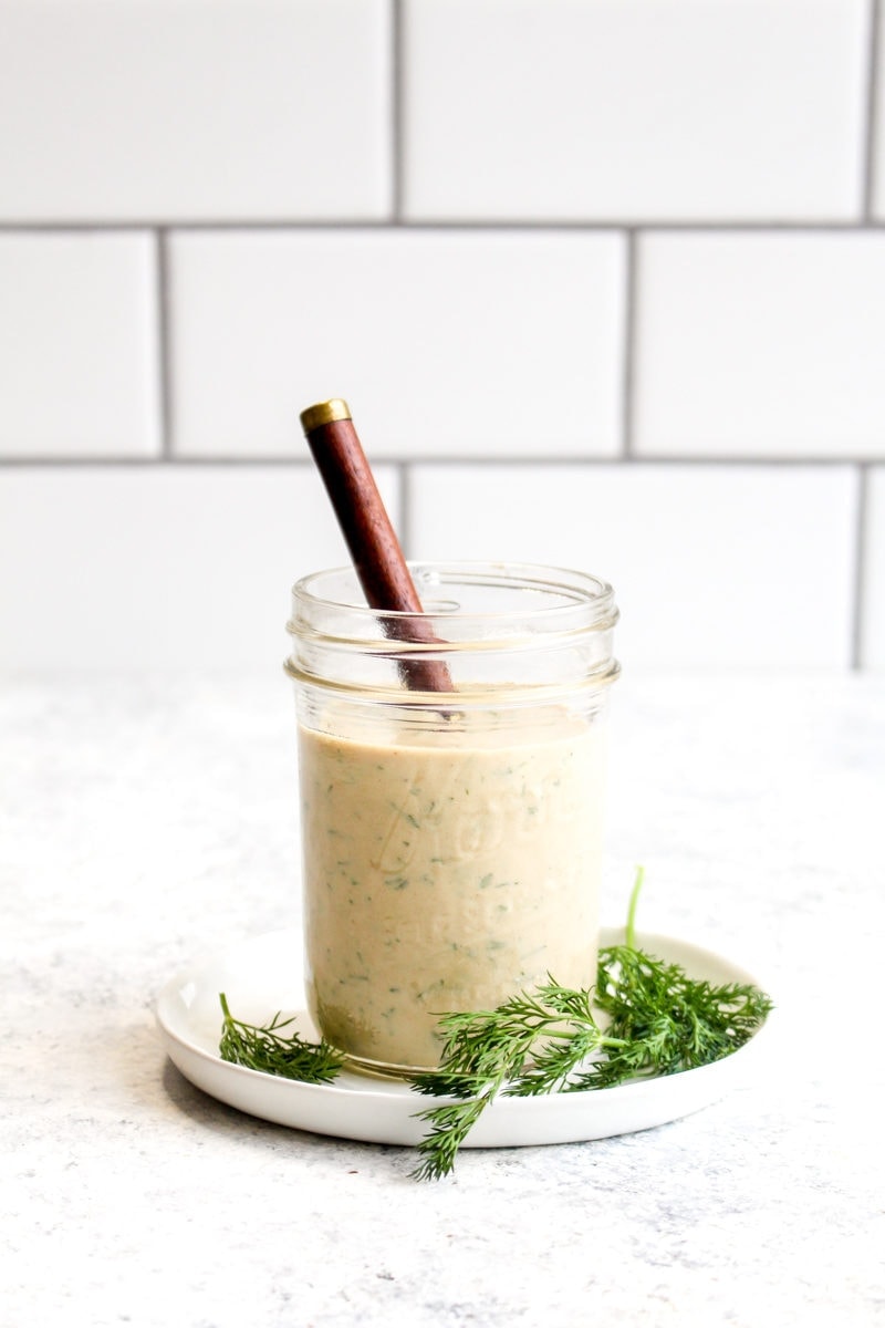 A glass jar of tahini ranch dressing with a wooden spoon.