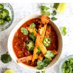 A bowl of vegan tortilla soup topped with tortilla strips and jalapeno slices.