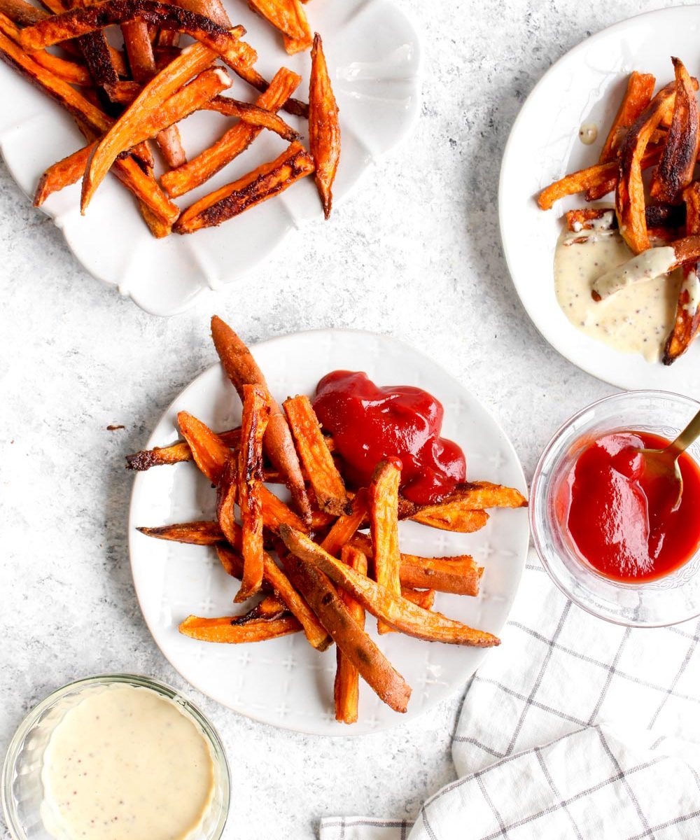 Seasoned sweet potato fries on a white plate with ketchup.