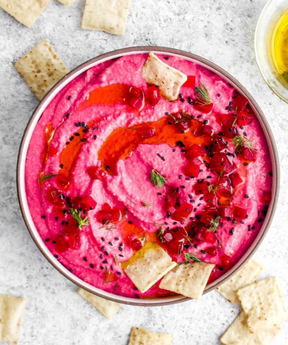 A bowl of pickled beet hummus with crackers.