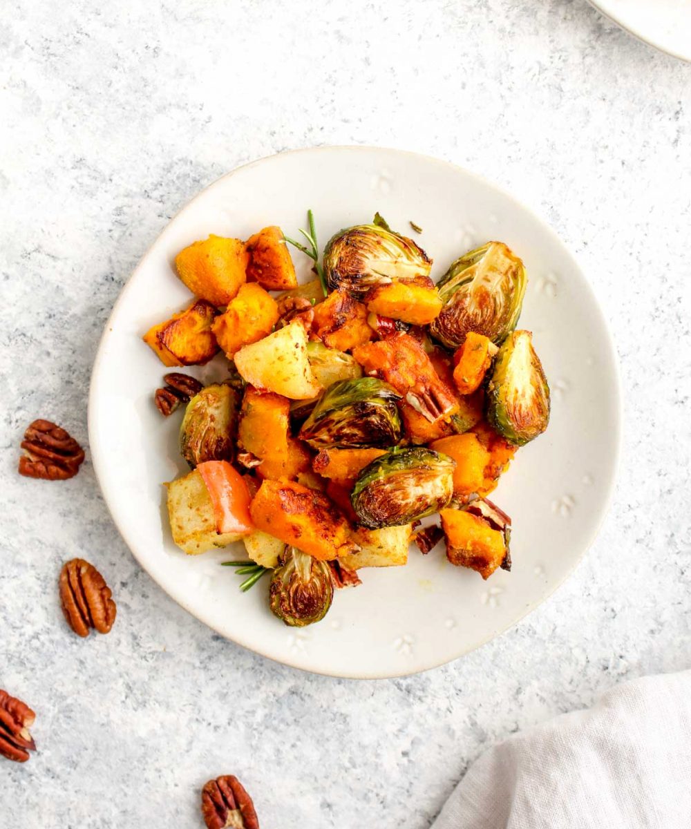 Butternut Squash, Apple, and Brussel Sprout Bake on a plate with rosemary and pecans.