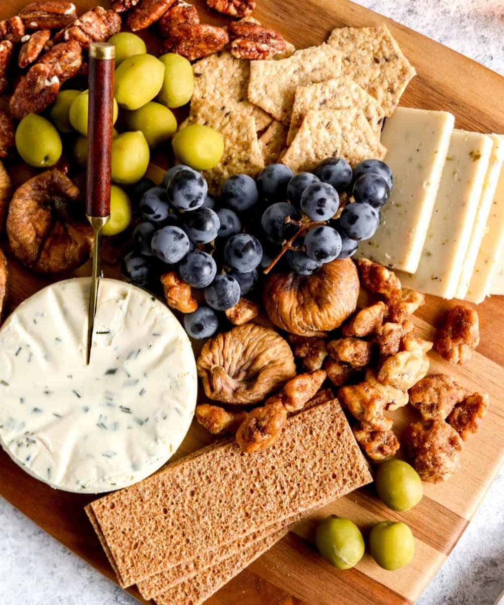 A vegetarian charcuterie board with crackers, dried figs, olives, glazed nuts and dairy free cheeses.