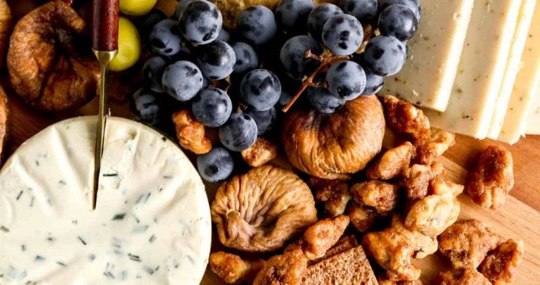 A vegetarian charcuterie board with crackers, dried figs, olives, glazed nuts and dairy free cheeses.