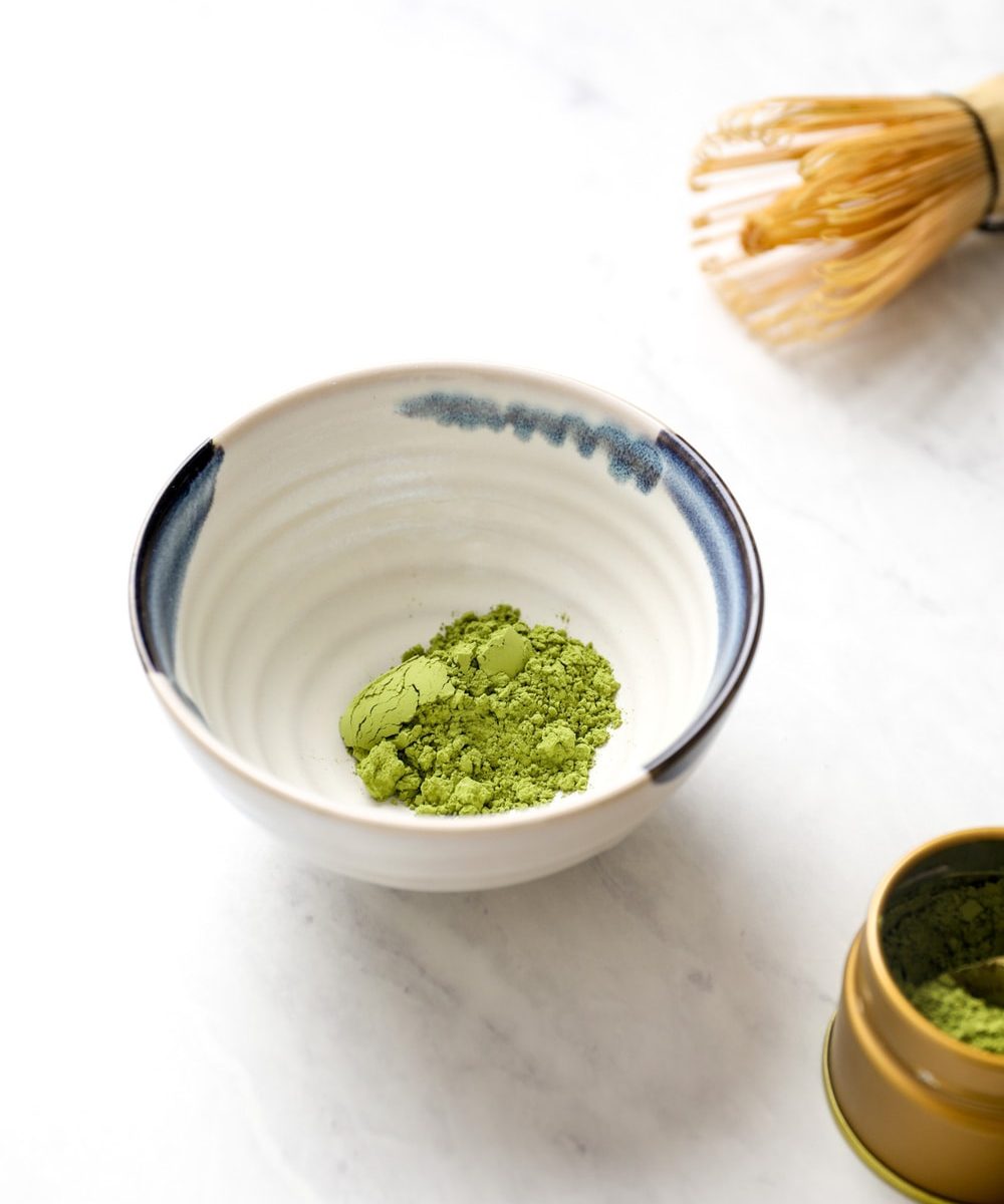 A matcha bowl filled with matcha powder with a whisk.