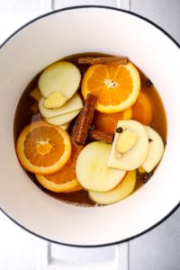 Apple cider, orange slices, apple, cinnamon, ginger, and allspice in a pot.