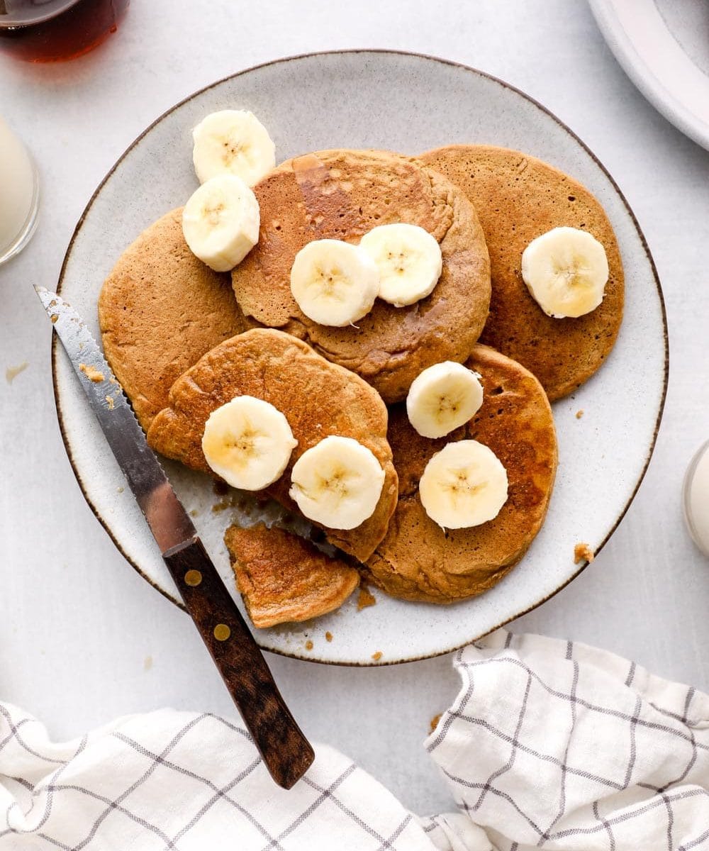 Oat Flour Pancakes on a plate with banana, maple, and cinnamon.
