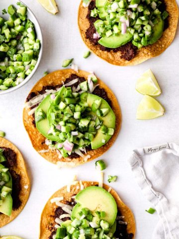 Avocado Tostadas with lime wedges on a grey surface.
