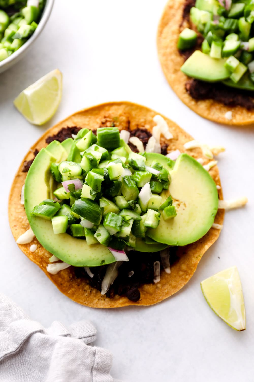 Avocado Tostada with vegan cheese, refried beans, and cucumber pico.