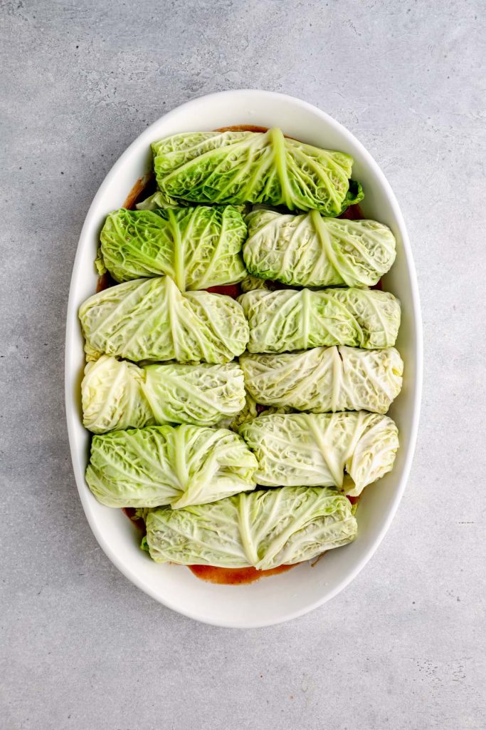 Rolled stuffed cabbage in a baking dish with tomato sauce.