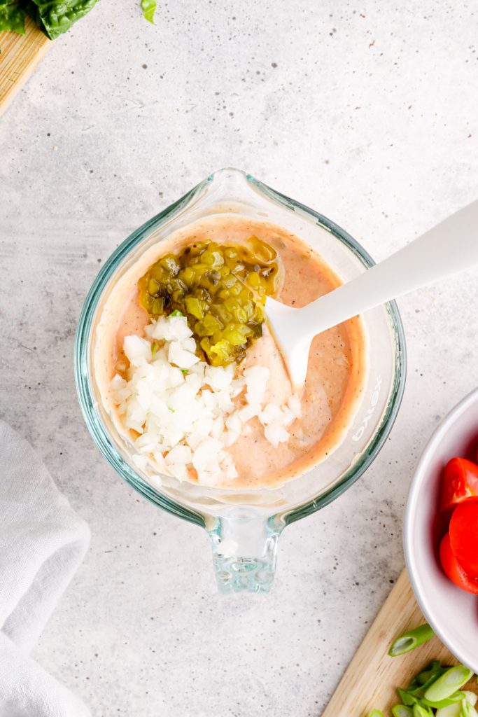 Minced onion and pickle relish being stirred into the creamy base of thousand island dressing.