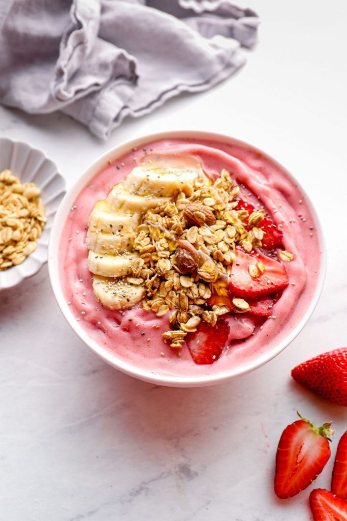 A strawberry smoothie bowl topped with strawberries, banana, and gluten free granola.