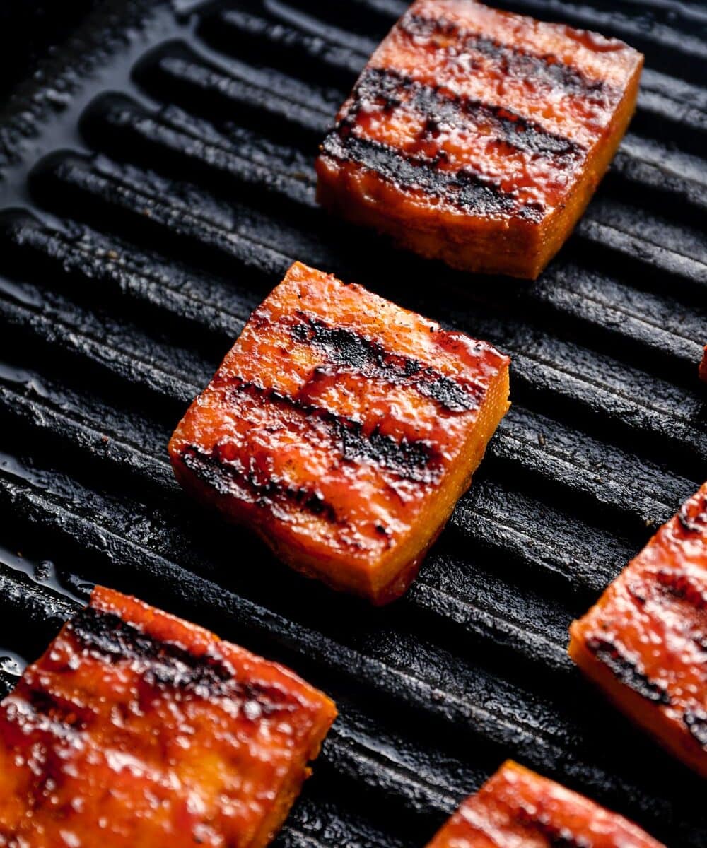 Smoked tofu with grill marks cooking in a grill pan.