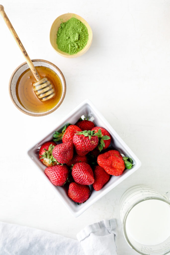 The ingredients to make a strawberry matcha latte: strawberries, honey, almond milk, and matcha powder.