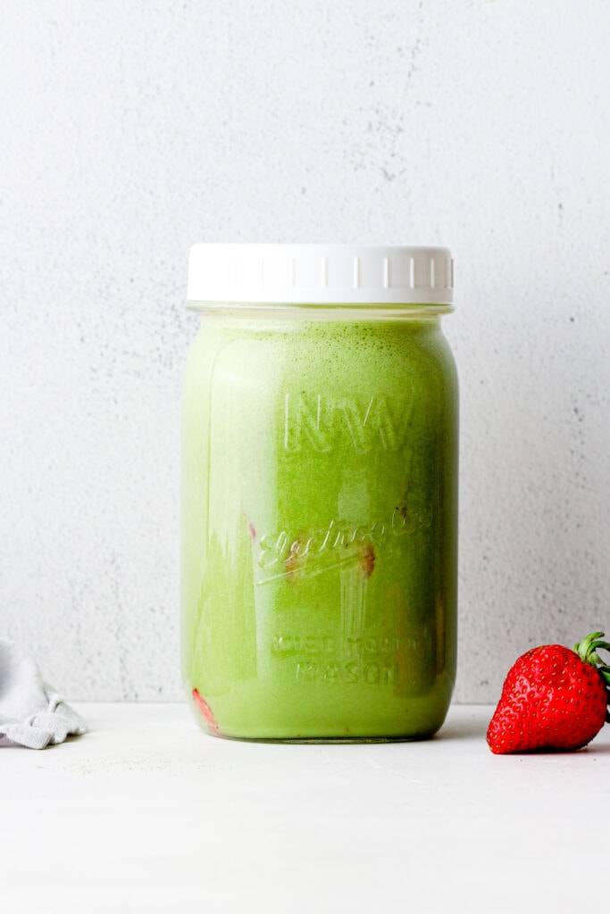A jar with matcha, honey, milk, and sliced strawberries.