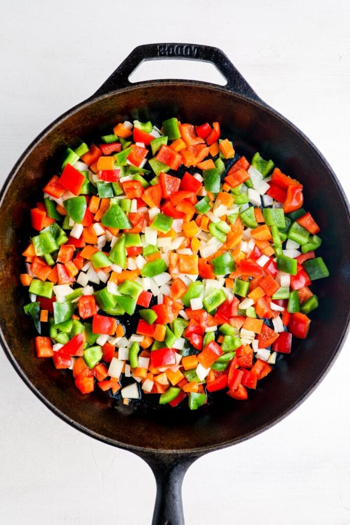 Onion, carrot, and bell pepper cooking in a skillet.