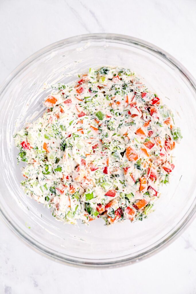 Vegetables and cream cheese mixed together in a glass bowl.