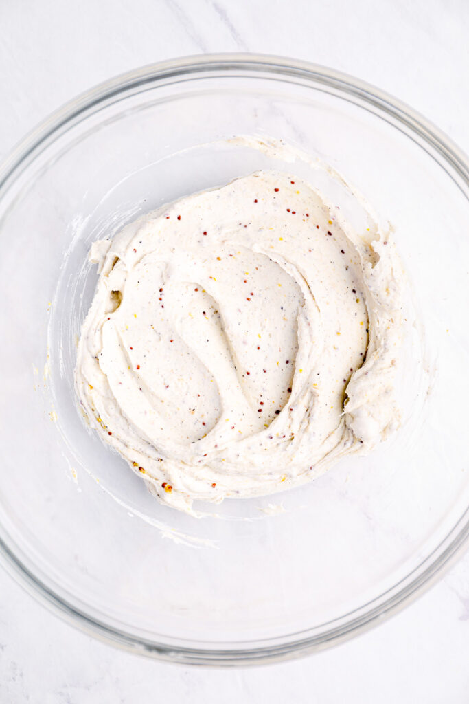 Cream cheese mixed with seasonings in a large glass bowl.