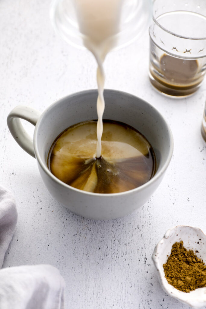 Steamed milk being poured into a glass of brewed hojicha tea.